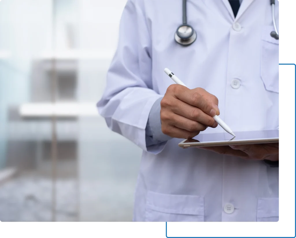 A doctor in a lab coat holds a tablet and writes with a stylus.
